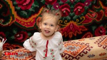 Little Mira, born in Luxembourg, wearing a traditional Moldovan blouse, against the backdrop of a traditional Moldovan carpet.