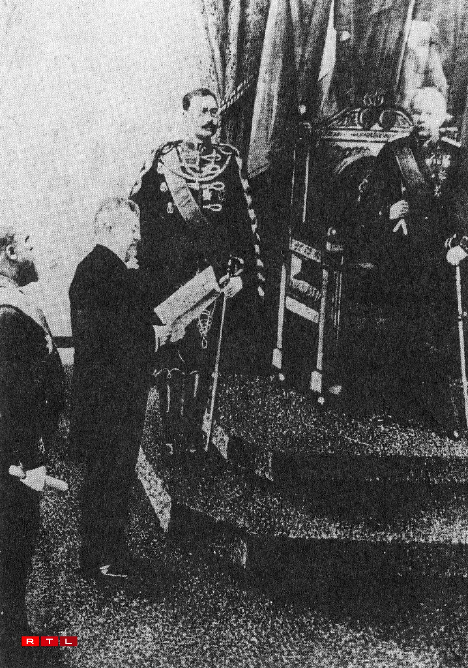 The image shows Duke Adolphe in his capacity as regent present at the Chamber of Deputies's oath-taking session on 11 April 1889. L.J Emmanuel Servais, then-president of the Chamber of Deputies, is reading whilst Adolphe's heir stands at his side.
