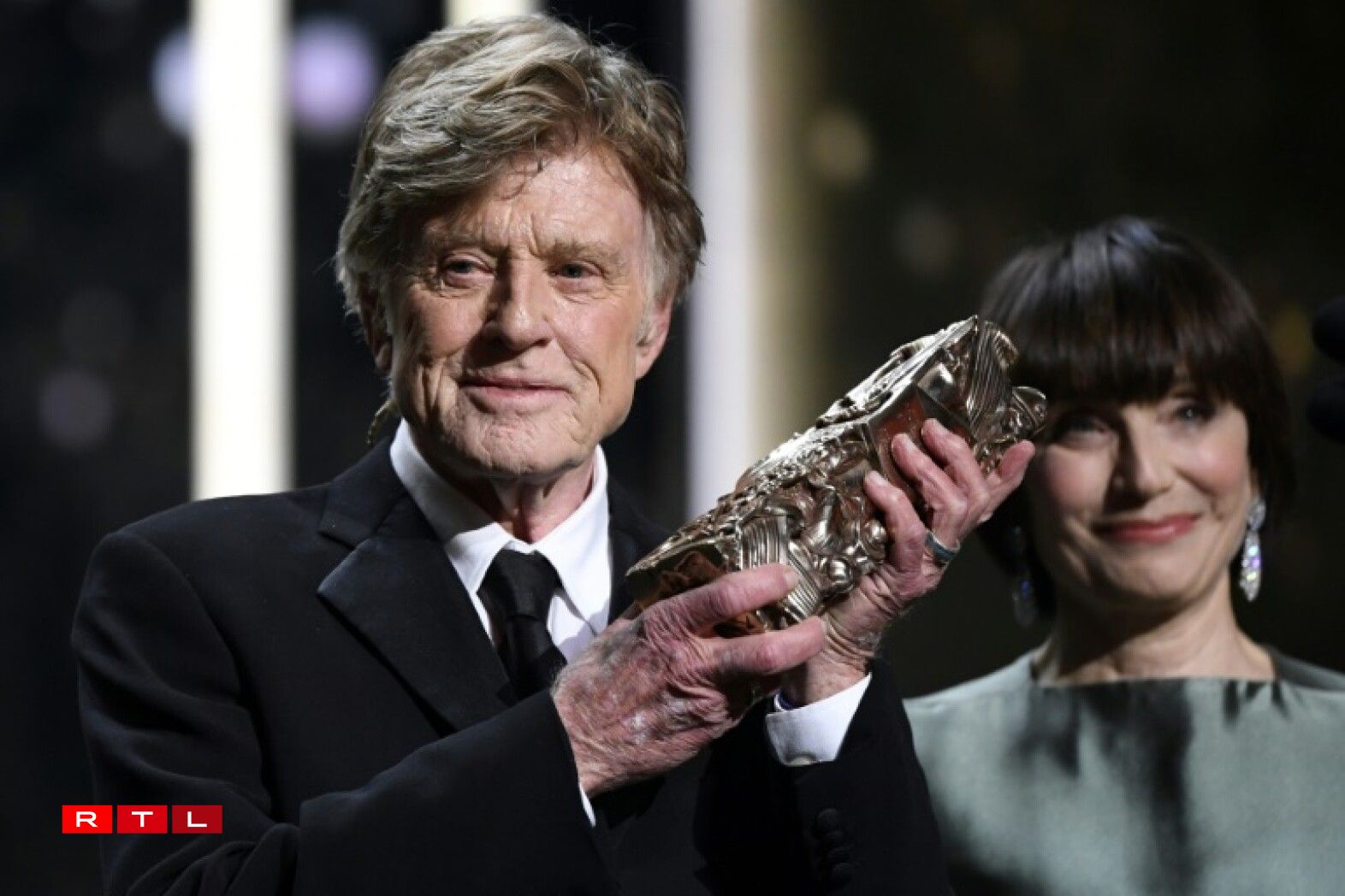 De Robert Redford mat sengem Präis, am Hannergrond déi britesch Presentatrice Kristin Scott Thomas.