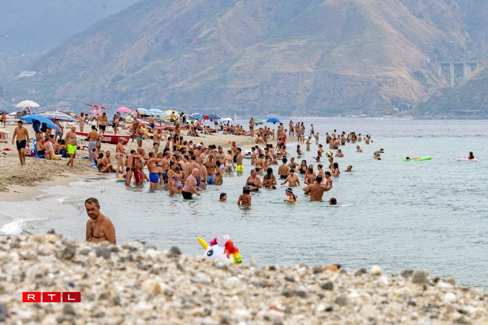 Les Italiens et les touristes se rafraîchissent dans l'eau sur une plage de Messine le 11 août 2021