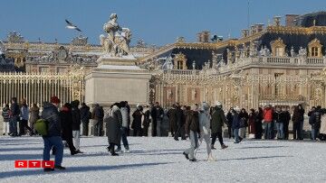 Des visiteurs se promènent dans la neige devant la "Grille d'Honneur", les portes dorées du château de Versailles.